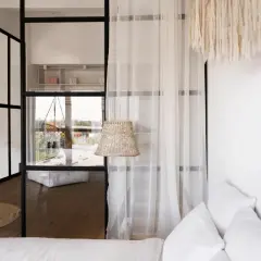 Jak urządzić pokój dzienny z sypialnią 20m2? Minimalistyczne wnętrze z przeszkloną ścianką, plecioną lampą i białymi tekstyliami.