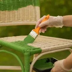 Ręka w rękawiczce maluje zieloną farbą do rattanu pleciony mebel.