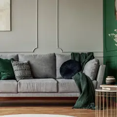 Elegancki salon w odcieniach butelkowej zieleni i szarości. Szara kanapa z zielonymi i szarymi poduszkami, zielony pled.