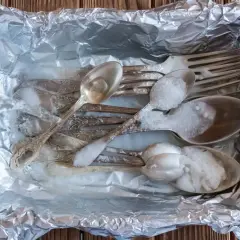 Jak wyczyścić poczerniałe sztućce? Woda z czajnika zalewa srebrne łyżki i widelce w folii aluminiowej, tworząc pianę.