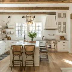 Jasna kuchnia modern farmhouse z drewnianymi belkami, wyspą i rattanowymi hokerami.